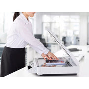 A woman in a white blouse and black skirt uses a white Epson DS-51000WN flatbed scanner in a bright office setting.